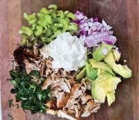 Shredded chicken salad ingredients with celery, red onion, avocado, and herbs